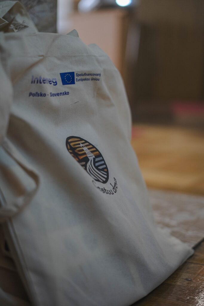 Biała torba promocyjna z logotypem programu i grafiką z napisem drogą drewna Biela reklamná taška s logom programu a grafikou s nápisom „Cesta dreva“