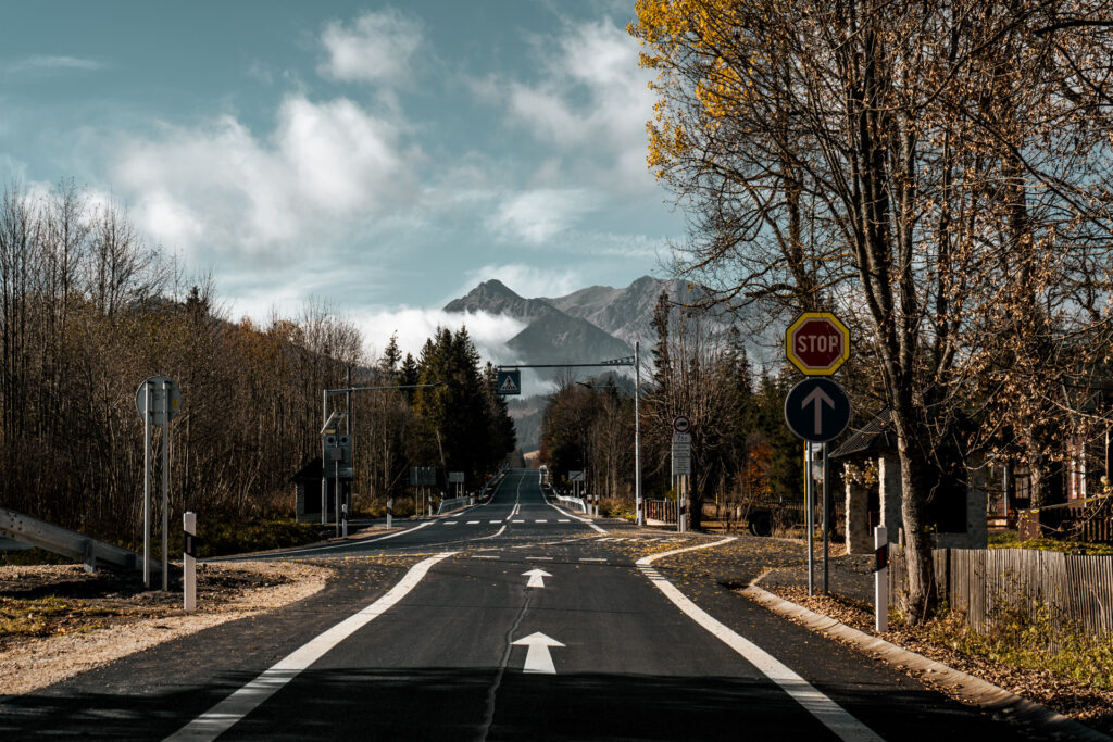 Skrzyżowanie drogi w nowym asfaltem, poboczami, przystankiem autobusowym. W tle góry przykryte mgłą Križovatka s novou asfaltovou cestou, krajnicami a autobusovou zastávkou. V pozadí sú hory zahalené hmlou