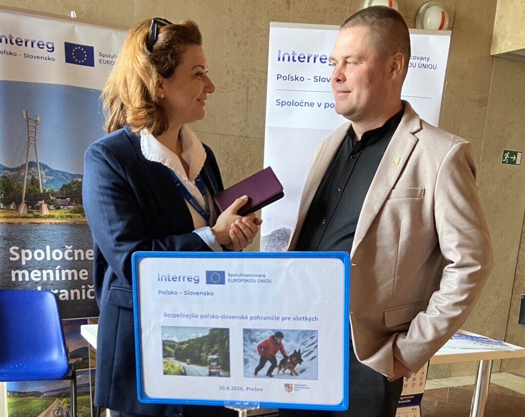 Kobieta z mężczyzną rozmawiają stojąc. Kobieta trzyma telefon, na którym nagrywa rozmowę Žena a muž sa rozprávajú v stoji. Žena drží v ruke telefón, na ktorom nahráva rozhovor